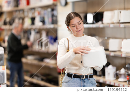 Positive young woman choosing toaster in hypermarket Positive young woman choosing toaster in hypermarket 139194312