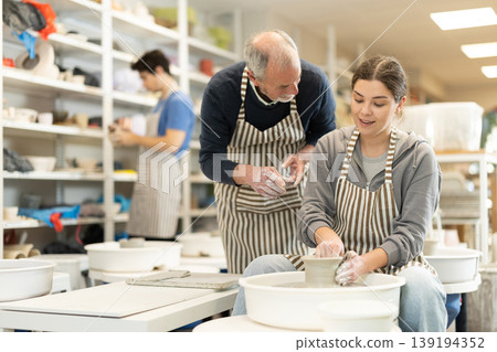 Mature man help to girl working on potters wheel in pottery workshop 139194352