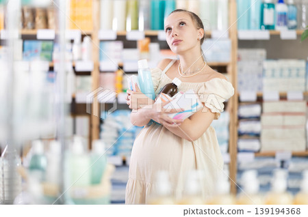Tired pregnant woman stands with armful of purchases of cosmetics and drugs in pharmacy Tired pregnant woman stands with armful of purchases of cosmetics and drugs in pharmacy 139194368