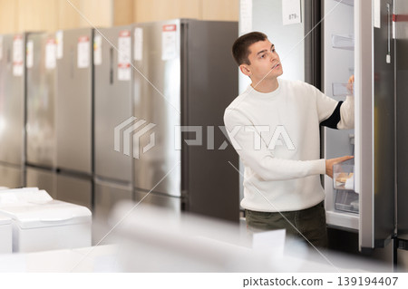 Guy choosing a refrigerator in an equipment store 139194407
