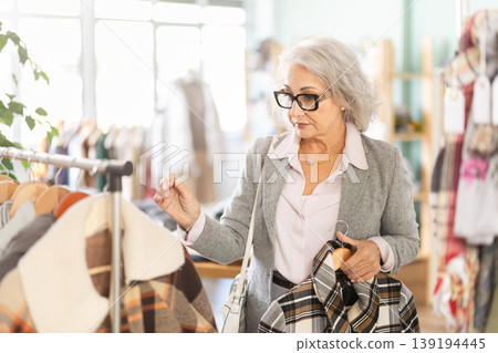 Family clothing store, senior woman customer chooses jacket or coat Family clothing store, senior woman customer chooses jacket or coat 139194445