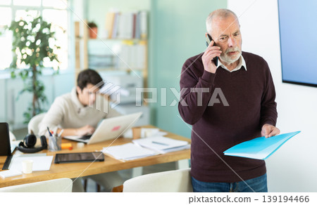 Senior man office male employee read documents and calling phone Senior man office male employee read documents and calling phone 139194466