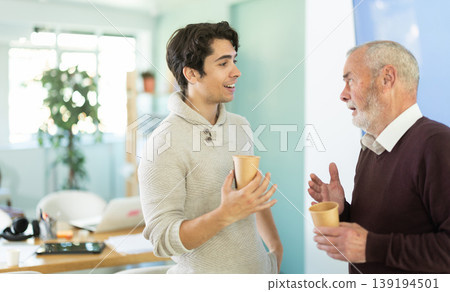 Young and elderly men colleagues drinking coffee in office Young and elderly men colleagues drinking coffee in office 139194501