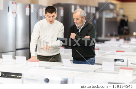 Elderly and young man choose washing machine or dishwasher Elderly and young man choose washing machine or dishwasher 139194545