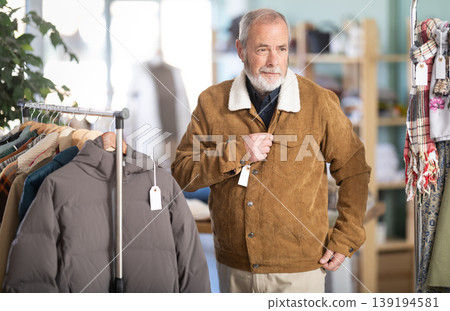 Elderly man trying on brown jacket in store 139194581