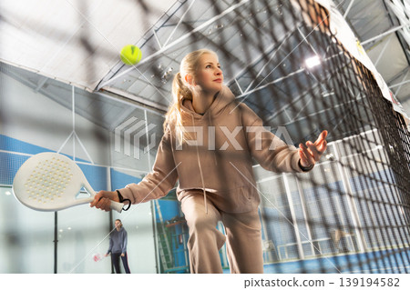 Sportive woman playing padel together with a partner. View through tennis net 139194582
