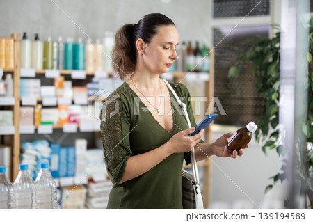 Middle-aged woman customer choosing syrup in drugstore Middle-aged woman customer choosing syrup in drugstore 139194589