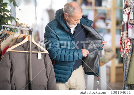 Mature male customer is trying on down jacket during shopping in store Mature male customer is trying on down jacket during shopping in store 139194631
