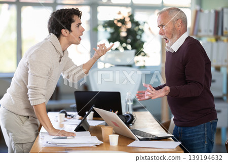 Elderly and young male colleague are arguing excitedly in office Elderly and young male colleague are arguing excitedly in office 139194632