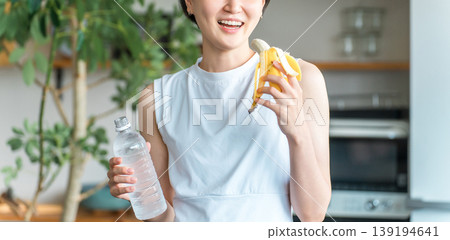 穿著運動服的亞洲年輕女子在廚房吃香蕉(訓練、補充能量、吃點心) 穿著運動服的亞洲年輕女子在廚房吃香蕉(訓練、補充能量、吃點心) 139194641
