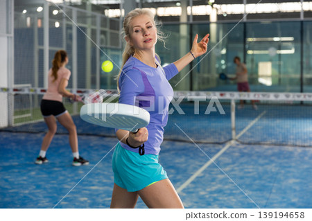 Positive female player hits ball while playing padel 139194658