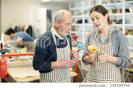 Young woman showing ceramic piece to elderly man Young woman showing ceramic piece to elderly man 139194744