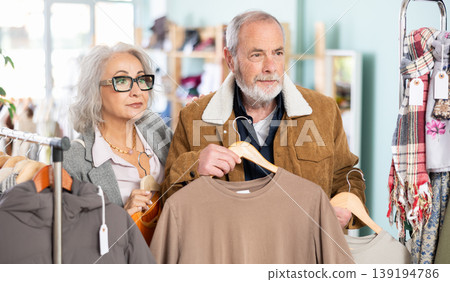 Mature married couple chooses fashionable t-shirt in clothing store Mature married couple chooses fashionable t-shirt in clothing store 139194786