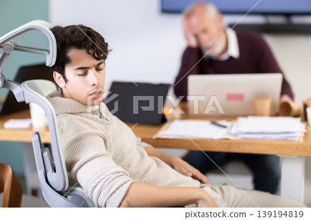 Tired elderly and young male colleagues fall asleep while working Tired elderly and young male colleagues fall asleep while working 139194819