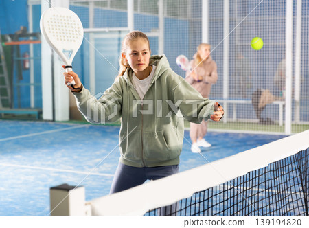 Padel game - teen girl actively kicks ball during a padel game Padel game - teen girl actively kicks ball during a padel game 139194820