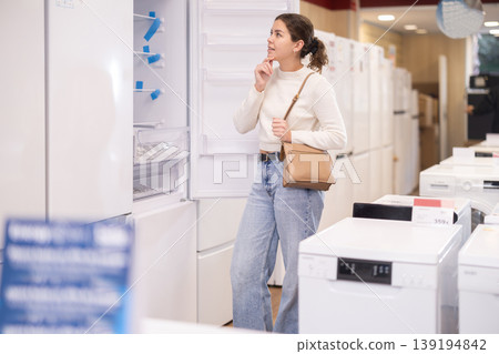 Young woman buyer examine fridge in detail before buying Young woman buyer examine fridge in detail before buying 139194842