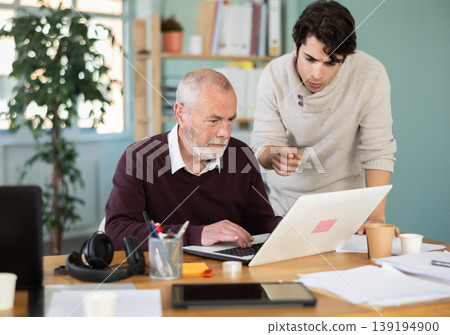 Young man helping elderly male colleague work on laptop Young man helping elderly male colleague work on laptop 139194900