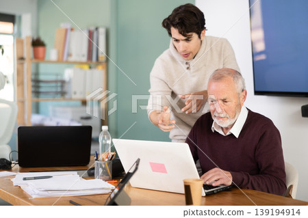 Guy helps elderly man complete task on laptop 139194914