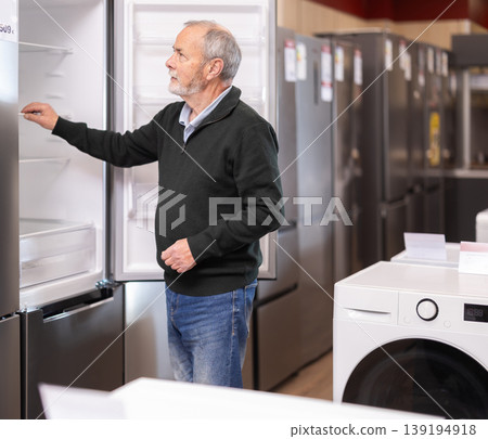 Elderly man choosing a large refrigerator in a store Elderly man choosing a large refrigerator in a store 139194918