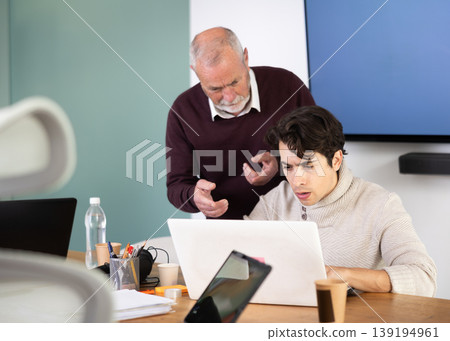 Mature male manager helping to guy during working at laptop in office Mature male manager helping to guy during working at laptop in office 139194961