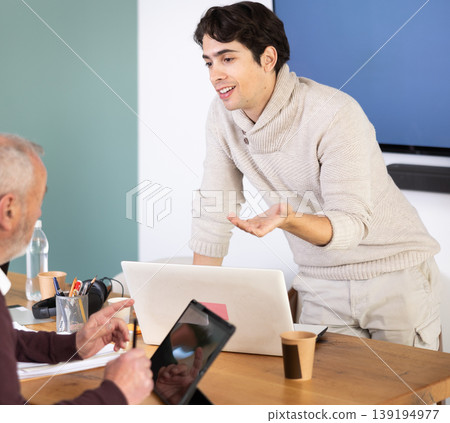 Elderly man working on tablet and young man on laptop in office Elderly man working on tablet and young man on laptop in office 139194977