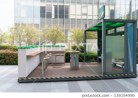 Outdoor smoking area in front of office building, modern design with glass-enclosed rooms and open deck. Outdoor smoking area in front of office building, modern design with glass-enclosed rooms and open deck. 139194990