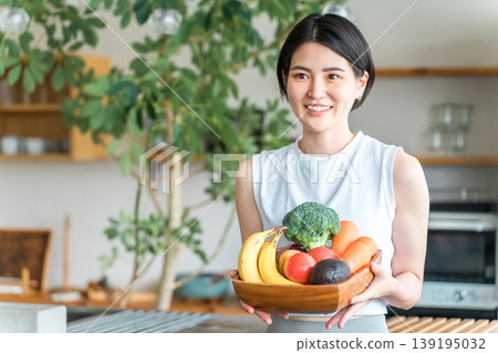 一位身穿運動服的年輕亞洲女性在廚房前拿著蔬菜（缺乏蔬菜、營養平衡、綠色和黃色蔬菜） 139195032