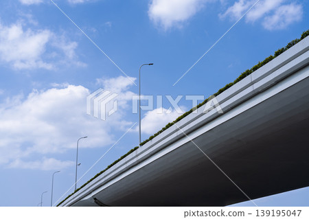 A perspective view of an elevated urban highway, with greenery and streetlights lining the blue sky. A perspective view of an elevated urban highway, with greenery and streetlights lining the blue sky. 139195047