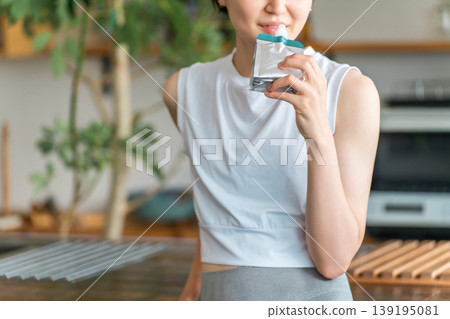 A young Asian woman in sportswear drinking jelly and replenishing her energy with nutritional supplement jelly A young Asian woman in sportswear drinking jelly and replenishing her energy with nutritional supplement jelly 139195081