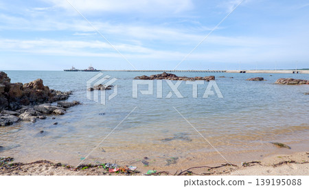 Calm Coastal Water with Distant Industrial Jetty and Rocks Calm Coastal Water with Distant Industrial Jetty and Rocks 139195088