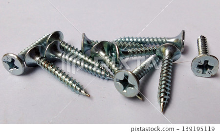 Shiny metal screws were scattered across the white surface. Shiny metal screws were scattered across the white surface. 139195119