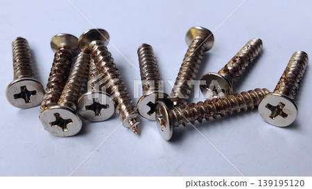 Shiny metal screws were scattered across the white surface. Shiny metal screws were scattered across the white surface. 139195120