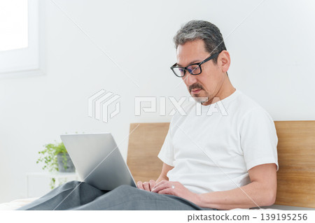 A middle-aged man using a computer in bed. 139195256