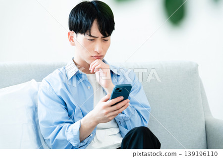 A man who uses a smartphone in the living room A man who uses a smartphone in the living room 139196110