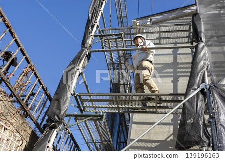 Residential construction workers performing exterior wall work on scaffolding. Residential construction workers performing exterior wall work on scaffolding. 139196163