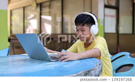 Smiling Asian Boy Using Laptop and Headphones for Happy Online Learning Outdoor Smiling Asian Boy Using Laptop and Headphones for Happy Online Learning Outdoor 139197168