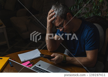 Thoughtful freelancer using smartphone while working on laptop 139197411