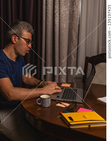 Tired freelancer drinking coffee while working late at night on laptop at home Tired freelancer drinking coffee while working late at night on laptop at home 139197435