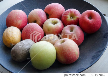 Assorted Fresh Apples and Two Kiwis, Lemons in a Dark Bowl on a White Table . Healthy Fruit Selection Assorted Fresh Apples and Two Kiwis, Lemons in a Dark Bowl on a White Table . Healthy Fruit Selection 139197862