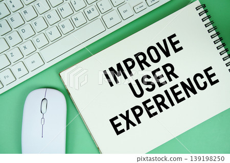 Notepad with the text "Improve User Experience" and white keyboard and wireless mouse on green background 139198250