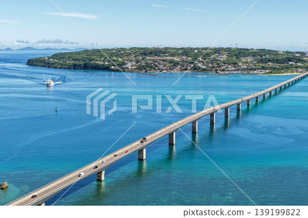 An August photograph taken from above, showing the Kouri Bridge and Kouri Island stretching across the emerald green sea in midsummer. 139199822