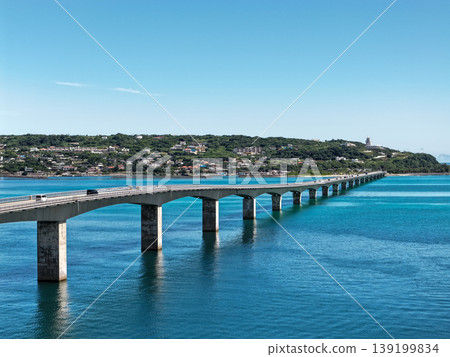 An August photograph taken from above, showing the Kouri Bridge and Kouri Island stretching across the emerald green sea in midsummer. 139199834
