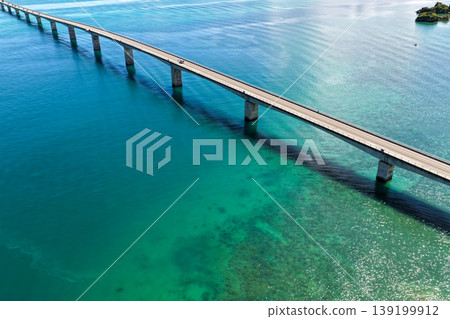 A photograph taken from the midsummer sky, showing the piers of the Kouri Bridge stretching out into the shallow, emerald-green sea. A photograph taken from the midsummer sky, showing the piers of the Kouri Bridge stretching out into the shallow, emerald-green sea. 139199912