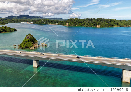A photograph taken from the midsummer sky, showing Kouri Bridge and a small island floating in the emerald green sea. A photograph taken from the midsummer sky, showing Kouri Bridge and a small island floating in the emerald green sea. 139199948