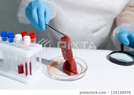 Scientist in protective gear holding lab-grown meat sample with tongs over petri dish in biotechnology lab. Cultured beef from in vitro cultivation process. Innovative sustainable protein production 139199976