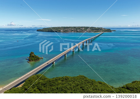 A photograph taken from the midsummer sky, showing the Kouri Bridge stretching across the emerald blue sea and Kouri Island. A photograph taken from the midsummer sky, showing the Kouri Bridge stretching across the emerald blue sea and Kouri Island. 139200018