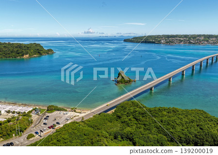 A photograph taken from the midsummer sky, showing the Kouri Bridge stretching across the emerald blue sea and Kouri Island. A photograph taken from the midsummer sky, showing the Kouri Bridge stretching across the emerald blue sea and Kouri Island. 139200019