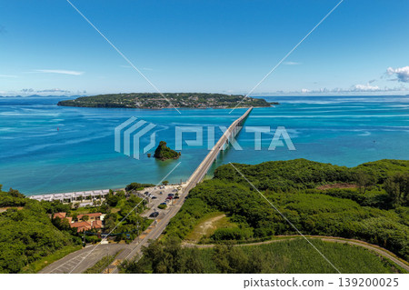 A photograph taken from the midsummer sky, showing the Kouri Bridge stretching across the emerald blue sea and Kouri Island. A photograph taken from the midsummer sky, showing the Kouri Bridge stretching across the emerald blue sea and Kouri Island. 139200025