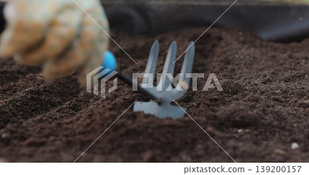 Farmer woman loosens soil with rake. Tillage, plant care, sowing. Agricultural concept. Young woman working in vegetable garden. Farmer woman loosens soil with rake. Tillage, plant care, sowing. Agricultural concept. Young woman working in vegetable garden. 139200157