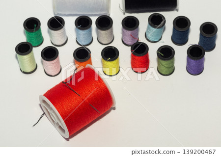 A spool of red thread with a needle, set against a background of spools of colored thread. A spool of red thread with a needle, set against a background of spools of colored thread. 139200467